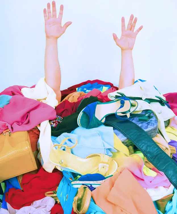 Woman's hands reaching out for help from a big pile of woman clothes