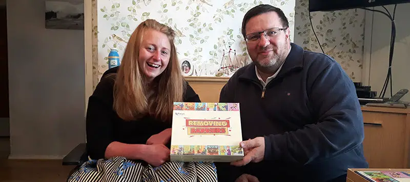 woman iwth long hair and a man with glasses and a beard hold a board game