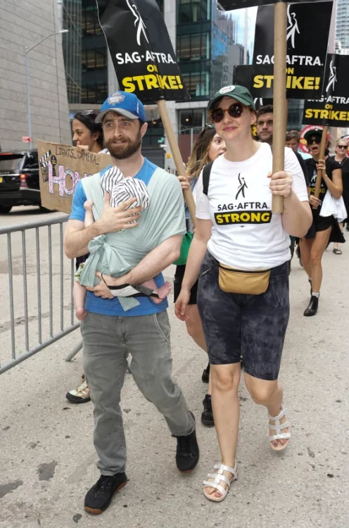 Daniel and his wife an baby at a protest, he is walking and has the baby in a papoose, he has a beard and baseball hat