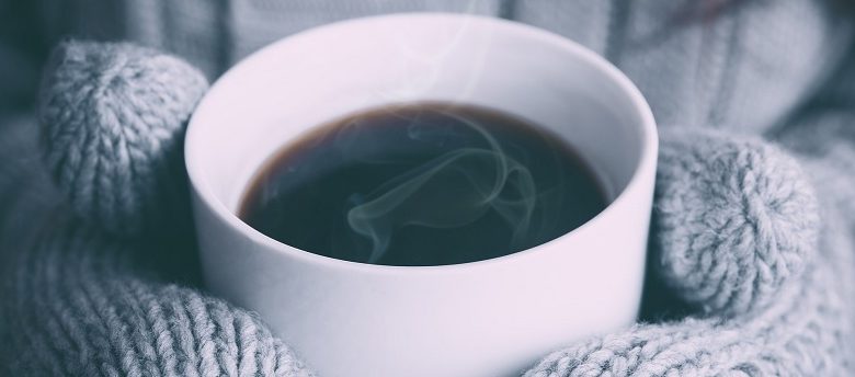 Mug of hot coffee being held by hands in wollen gloves