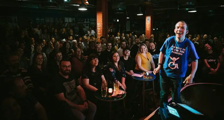 Lost Voice Guy on stage with audience in background