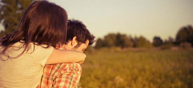 Woman hugging a man from behind walking across a field