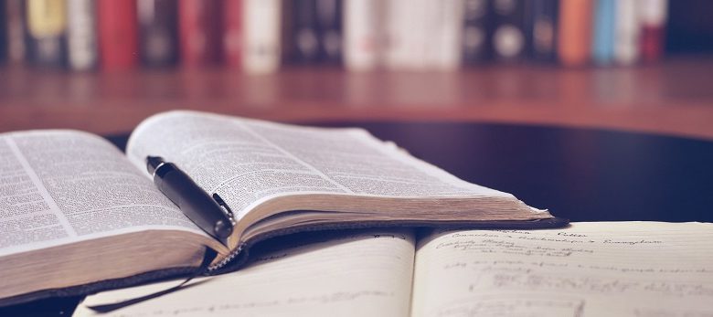 Open books in a library with a pen on top