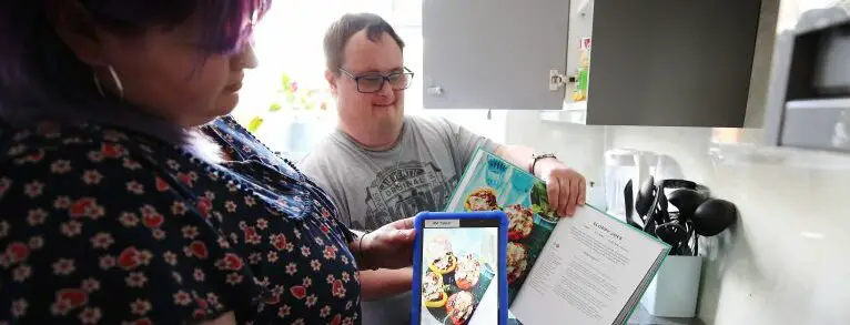 Man with Downs Syndrome looking at app MyLife app in kitchen with carer