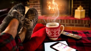 Legs in slippers resting on a footstall with a phone, TV remote and tablet on in front of a fire