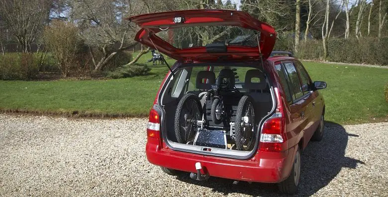 Mountain Trike wheelchair folded into the open boot of a red car