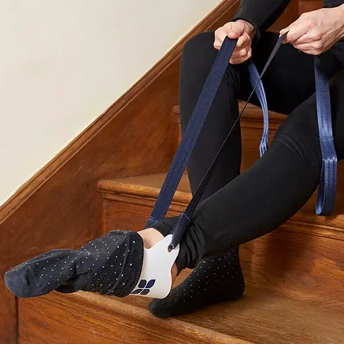 Navy sock dressing aid being used to put on a white sock by a woman sat on the stairs