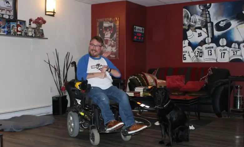 Alex in his living room with his black Labrador dog