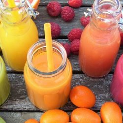 Colourful smoothies with straws in a row surrounded by fruit