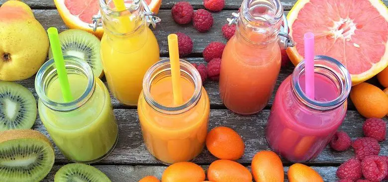 Colourful smoothies with straws in a row surrounded by fruit