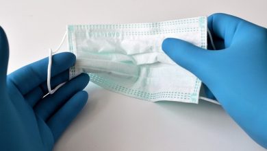 Face mask being held between two hands in blue plastic gloves