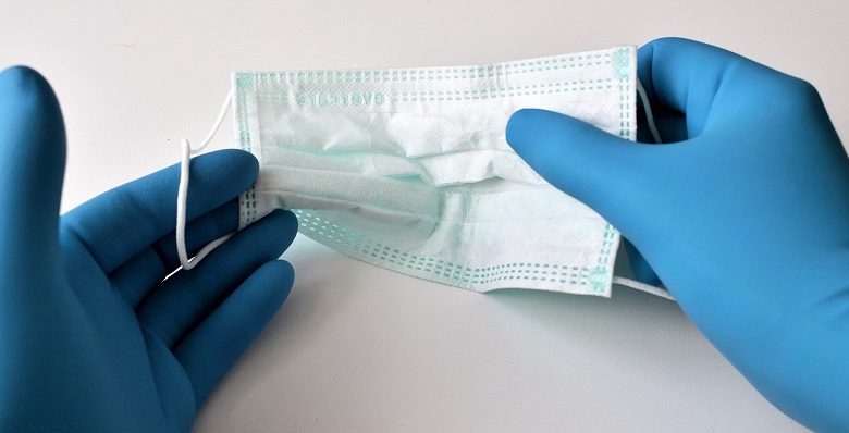 Face mask being held between two hands in blue plastic gloves