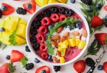 Fruit, rice, nuts and yogurt in a bowl on a white table surrounded my fruit