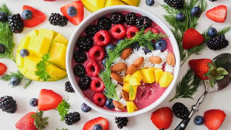 Fruit, rice, nuts and yogurt in a bowl on a white table surrounded my fruit