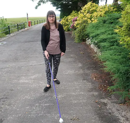 Holly walking with her cane on a path next to bushes