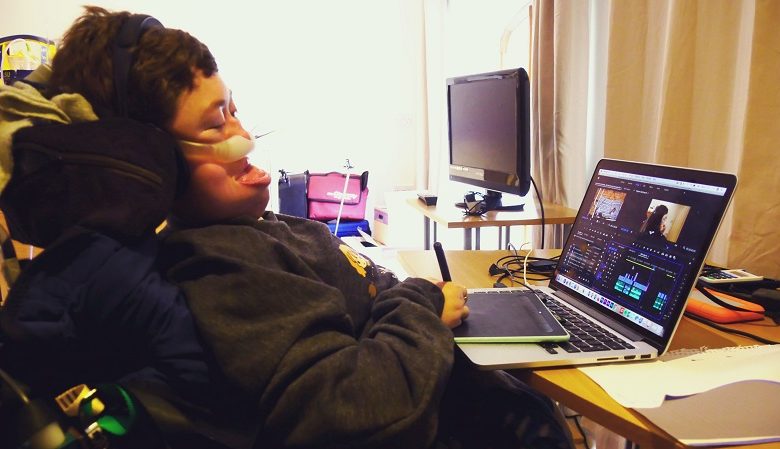 Stephanie Castelete-Tyrrell in her wheelchair at her laptop on a desk editing a film