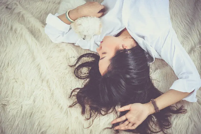 Woman sleeping on a fake fur rug with a small white dog