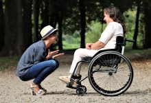 Two friends smiling next to each other, one in a wheelchair and one squatting down.