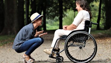 Two friends smiling next to each other, one in a wheelchair and one squatting down.