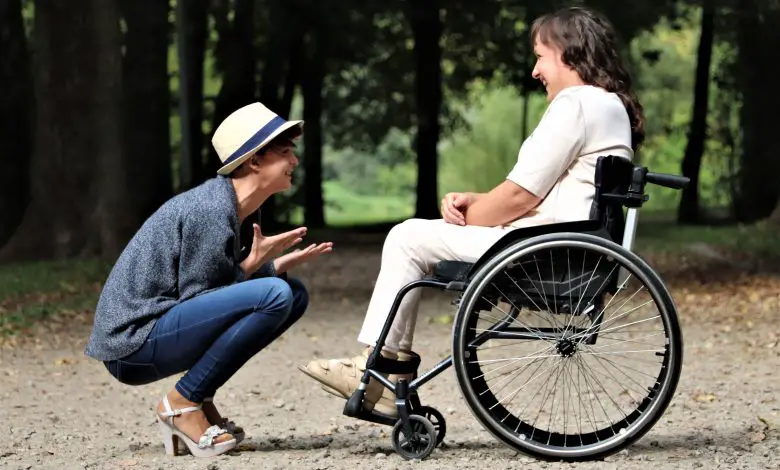 Two friends smiling next to each other, one in a wheelchair and one squatting down.