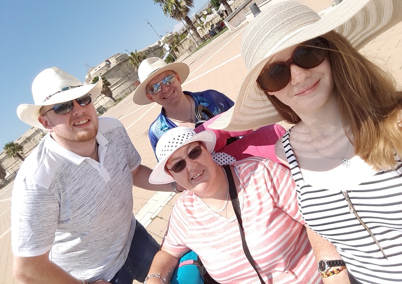 Caroline in her wheelchair with her two children and husband on holiday all wearing hats