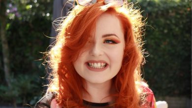 Close up of Lucy Edwards outside with red hair and eyeshadow wearing sunglasses on her head