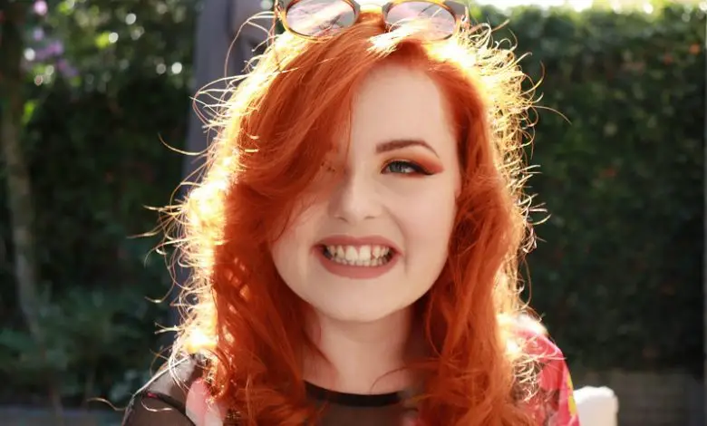 Close up of Lucy Edwards outside with red hair and eyeshadow wearing sunglasses on her head