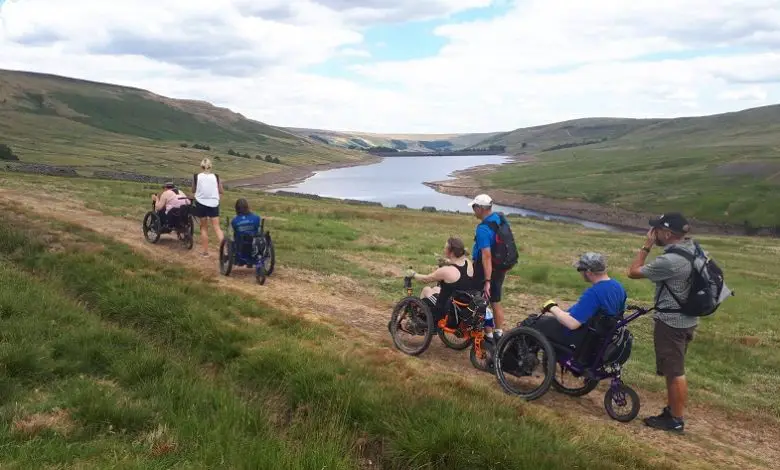 Group of disabled people in all-terrain wheelchairs next to Scar House Reservoir