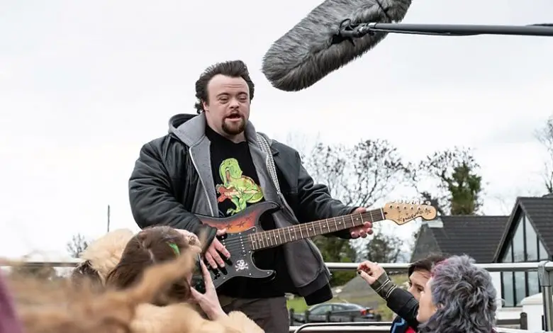 James Martin holding a guitar at a music festival in the film Ups and Downs