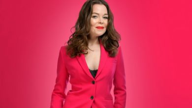 Juliette Burton in a pink suit and white heeled shoes stood on a pink background