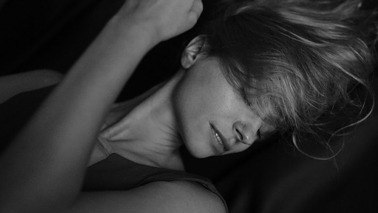 Black and white image of a woman lying on a black silk sheet with her eyes closed and hair across her face