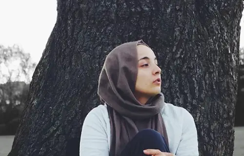 Lina Bettayeb wearing a brown hijab sat on the ground in front of a tree
