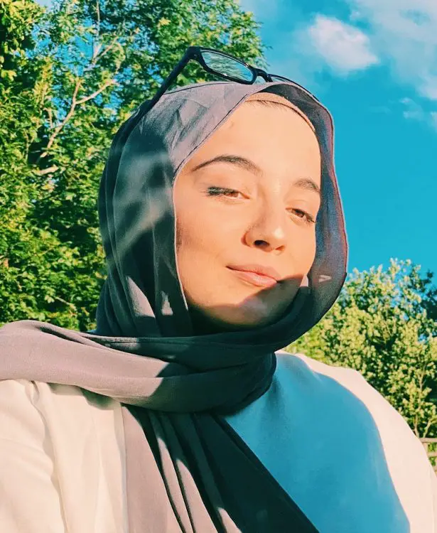 Lina Bettayeb wearing a grey hijab stood in front of a tree looking into the distance.