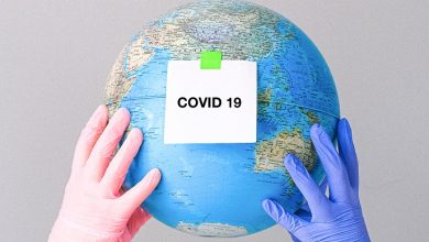 Two hands wearing gloves holding a globe with the word Covid on a post it note