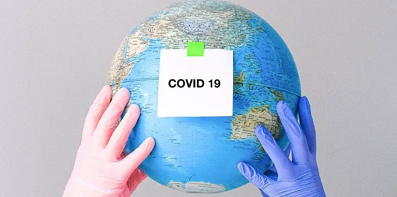Two hands wearing gloves holding a globe with the word Covid on a post it note