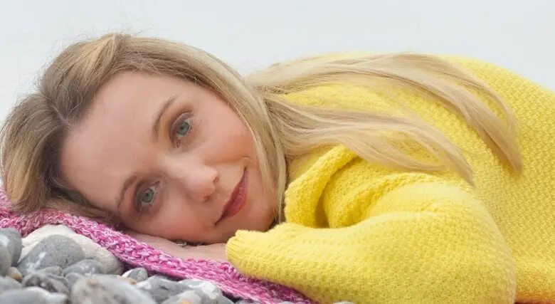 Cerrie Burnell in a yellow jumper lying on woolen pink and grey blankets