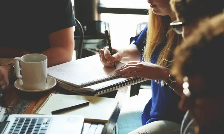 Four people at work dressed smartly sat around a table with laptops, pads and pens having a meeting