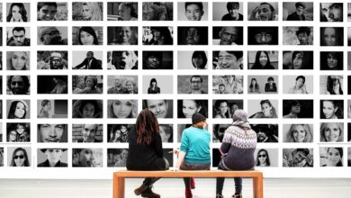 Three people sat on a bench in front of a wall of black and white portraits of people