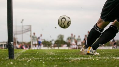 A football flying toward a goal and a goal keeper ducking out of the way