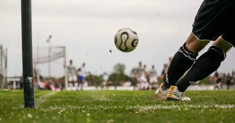 A football flying toward a goal and a goal keeper ducking out of the way