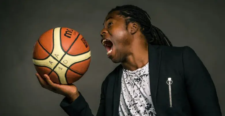 Ade Adepitan holding a basketball as if he is going to eat it