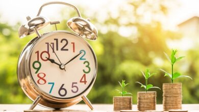 Three piles of coins with shoots growing from them next to a clock