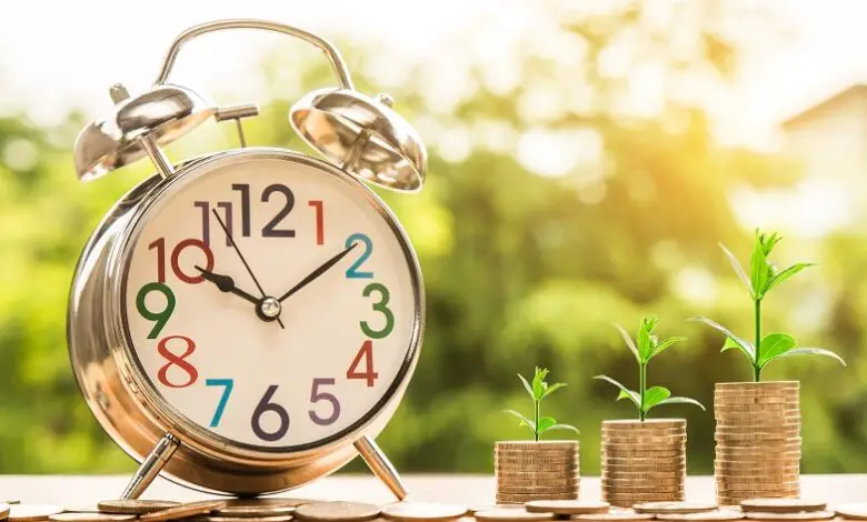 Three piles of coins with shoots growing from them next to a clock