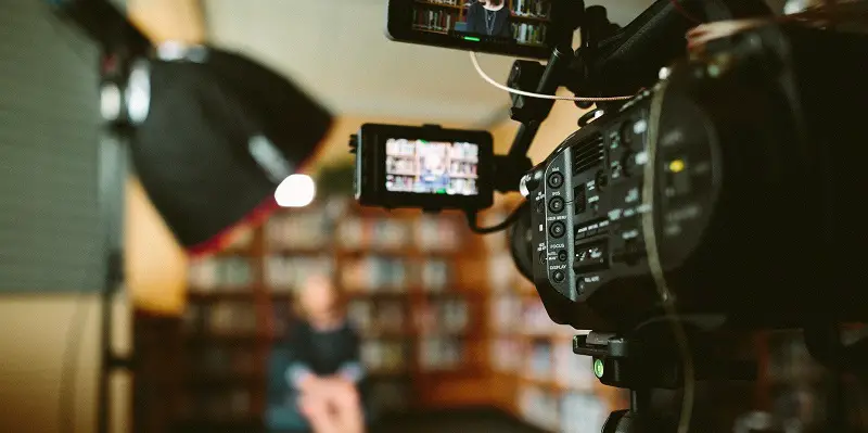 View from behind a camera filming a woman sat in a library