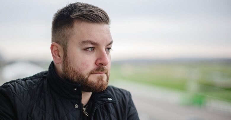 Alex Brooker in a black jacket viewed from the side looking into the distance