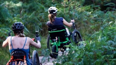 Laura May in her Mountain Trike wheelchair leading another woman in her wheelchair through shrubland