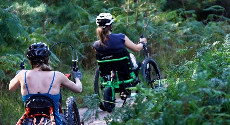 Laura May in her Mountain Trike wheelchair leading another woman in her wheelchair through shrubland