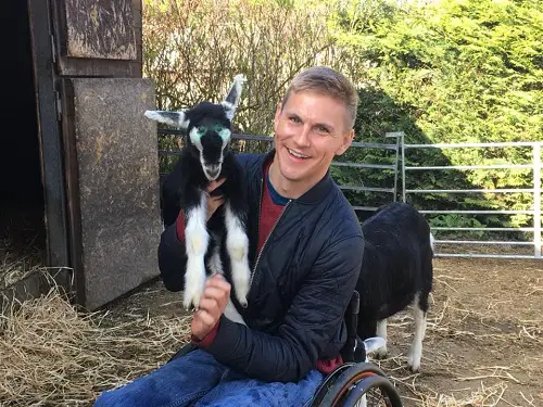 Steve Brown on a farm sat in his wheelchair holding a black and white goat