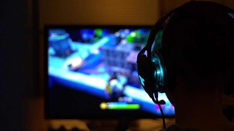 A gamer viewed from behind playing a video game on a television in a dimly lit room
