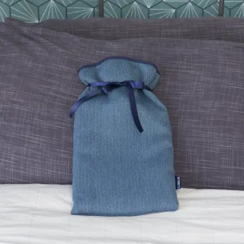 https://shop.disabilityhorizons.com/products/disability-aids-uk-for-the-home/hot-water-bottle/ Hot water bottle in a soft blue cover with a satin ribbon sat on a bed prodded up against grey cushions